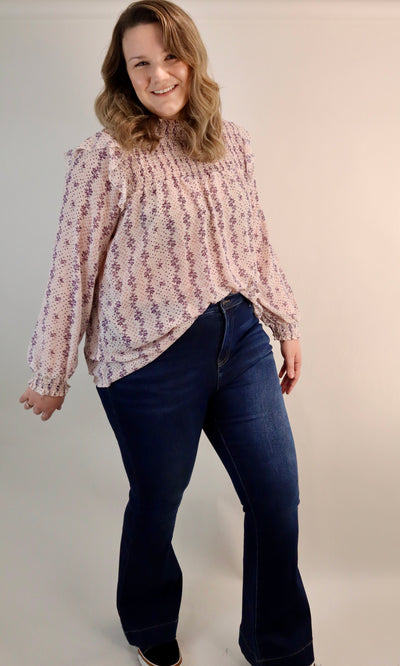 Women's curvy floral blouse with smocking details at the top and ruffles at the shoulder. Pink and purple make up this cream lightweight blouse. Plus sizes available 