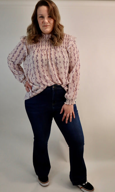 Women's curvy floral blouse with smocking details at the top and ruffles at the shoulder. Pink and purple make up this cream lightweight blouse. Plus sizes available