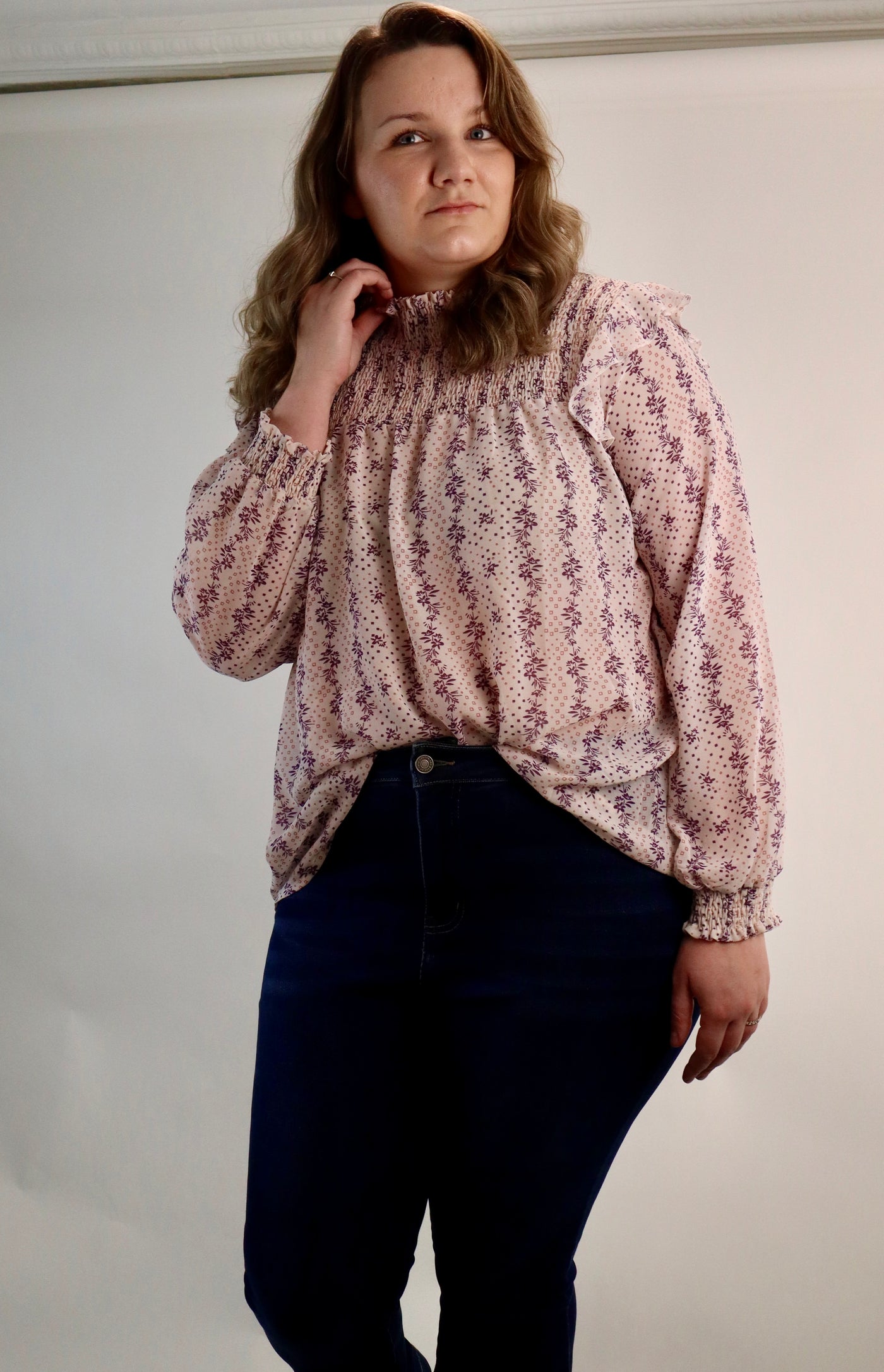 Women's curvy floral blouse with smocking details at the top and ruffles at the shoulder. Pink and purple make up this cream lightweight blouse. Plus sizes available